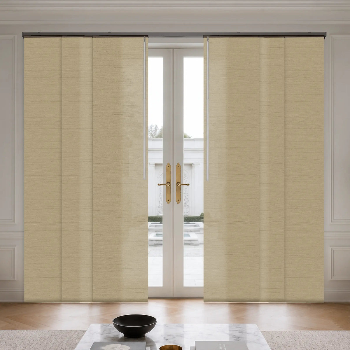 Two-panel beige textured rollerback curtains hanging on a black rod in front of white double glass doors, shown in a bright, modern room with a marble coffee table and wooden floor.
