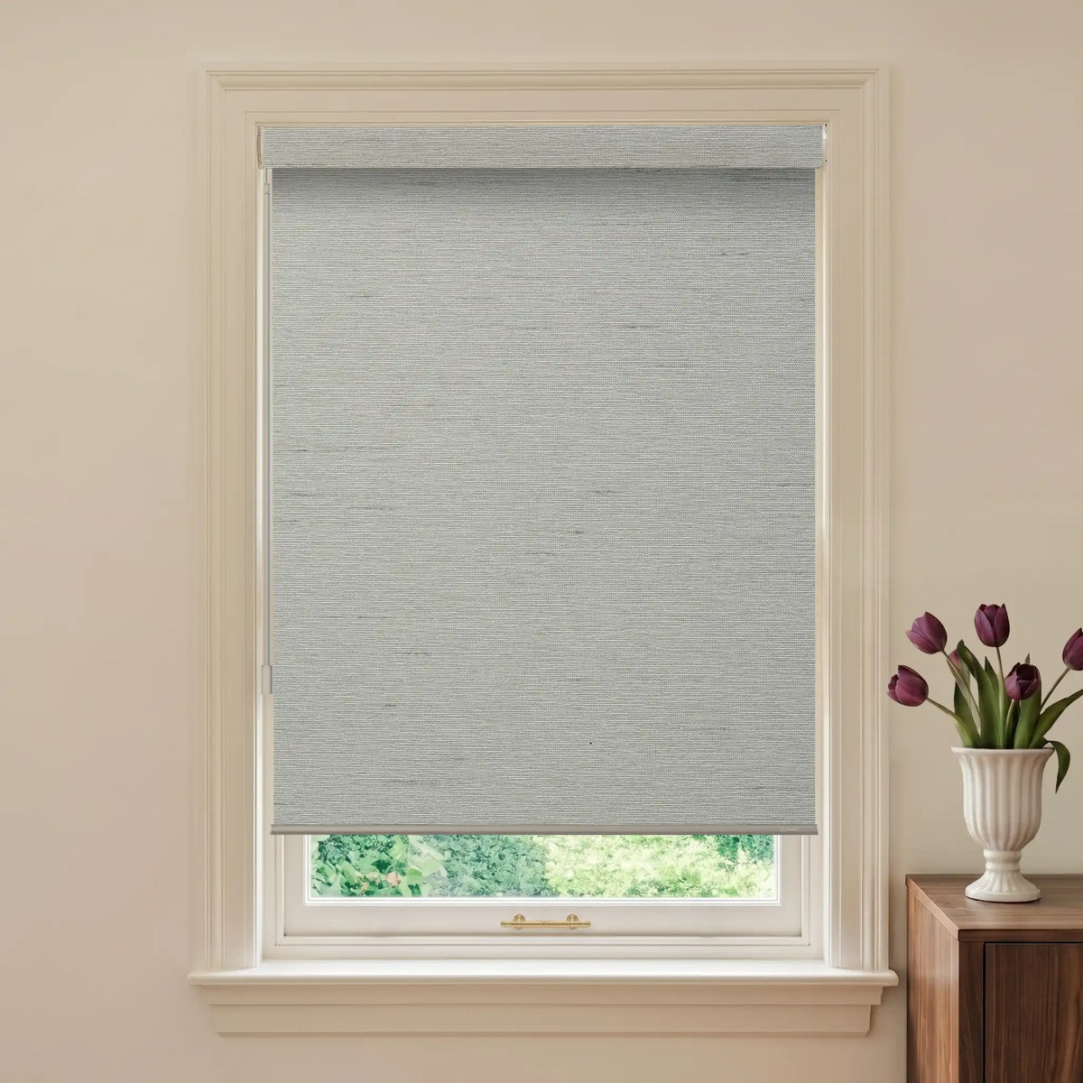 Window with a gray roller blind and a vase of purple tulips on a wooden cabinet.