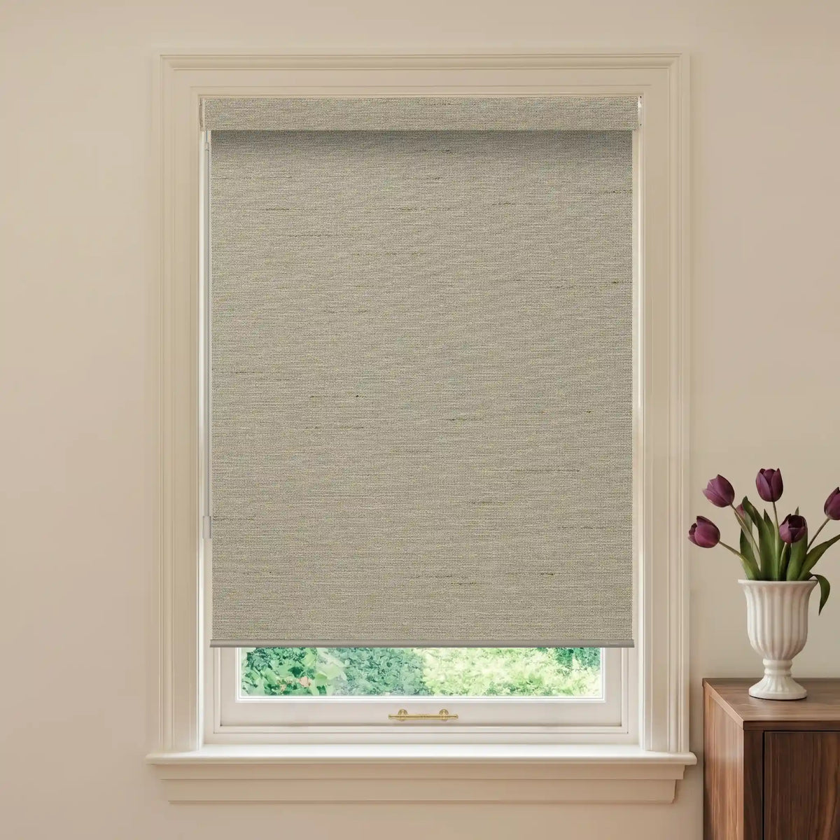 Window with a gray roller blind and a vase of purple tulips on a wooden side table.