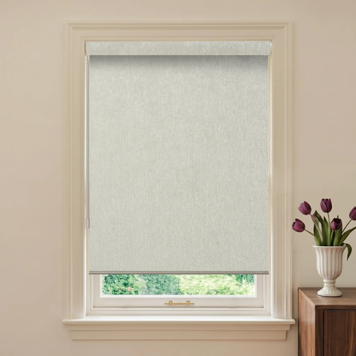 Window with light gray roller blind and a vase of purple tulips on a wooden cabinet.