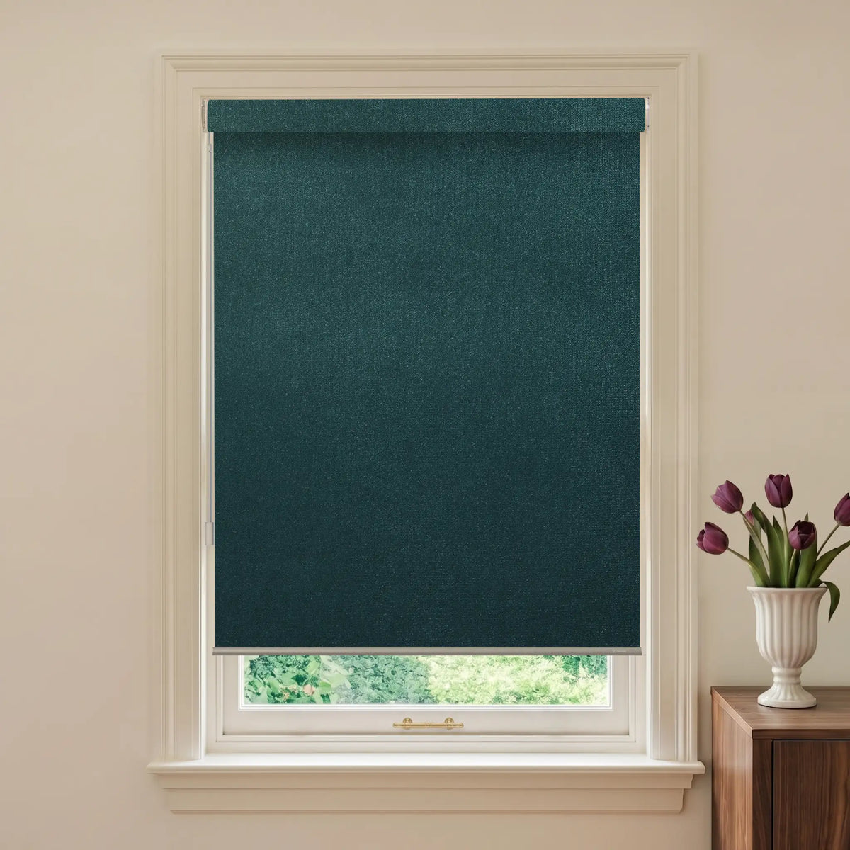 Teal roller blind on a window with a vase of tulips on a nearby table.