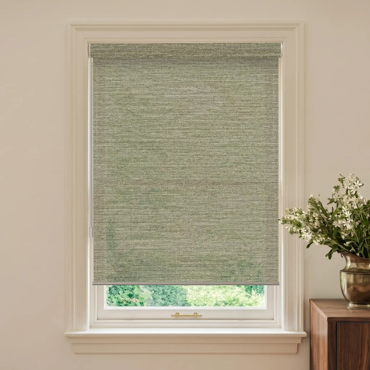 Window with a green woven blind and a vase of flowers on a table.