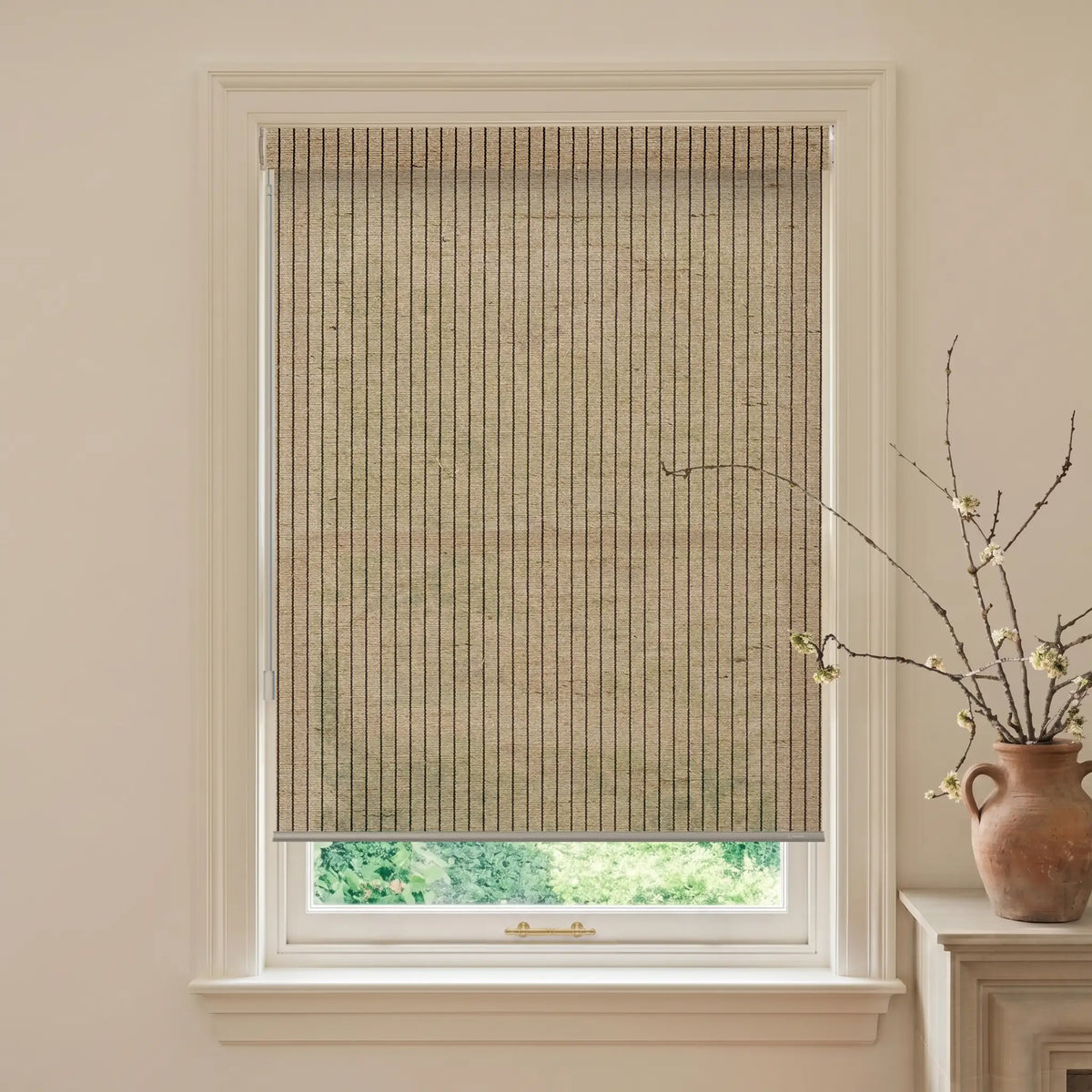 Window with a woven blind, light-colored wall, and a vase with branches on a windowsill.