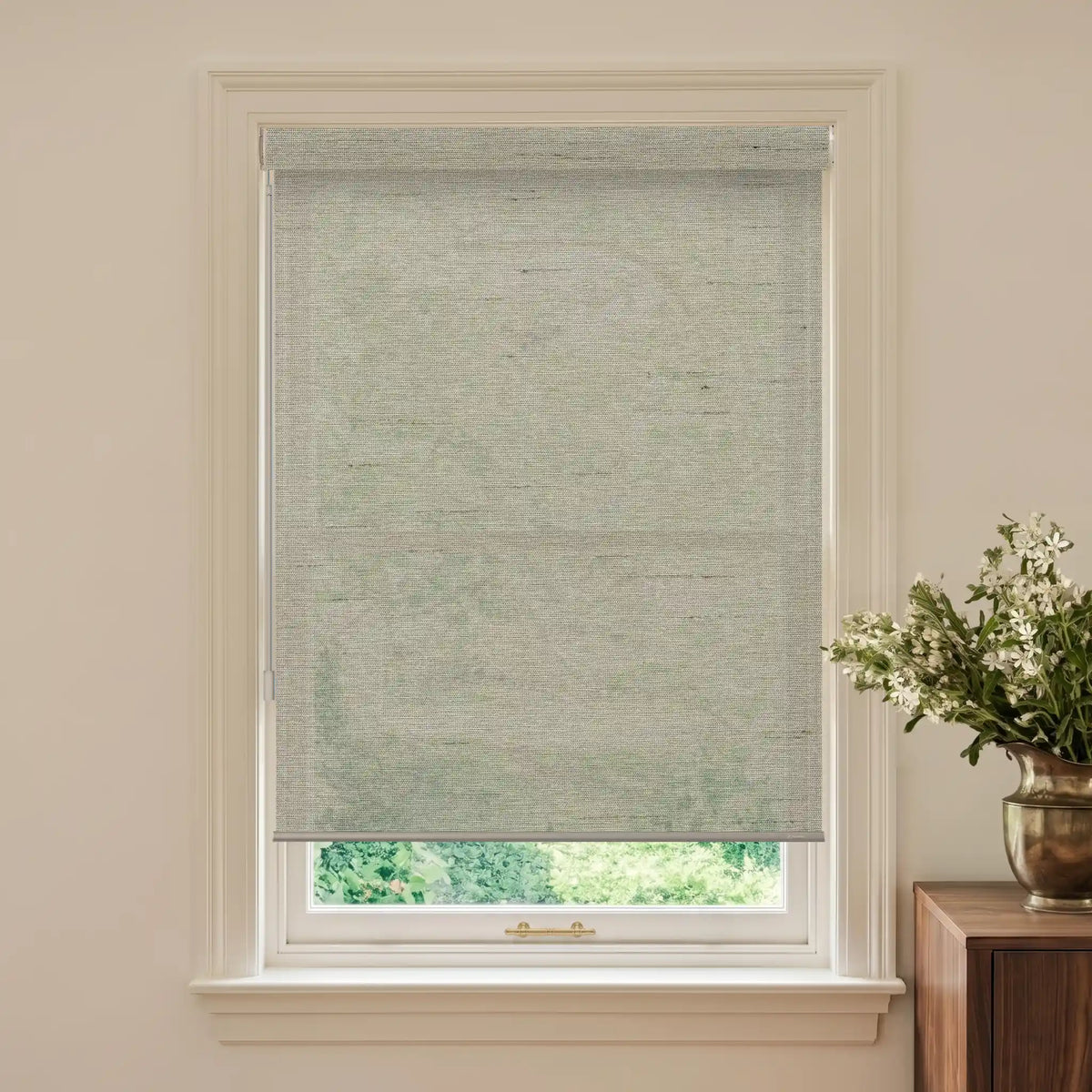 Window with a gray roller blind and a vase of flowers on a wooden cabinet.