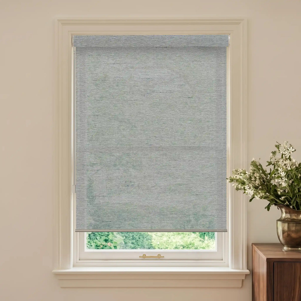 Window with a gray roller blind and a vase of flowers on a wooden cabinet.