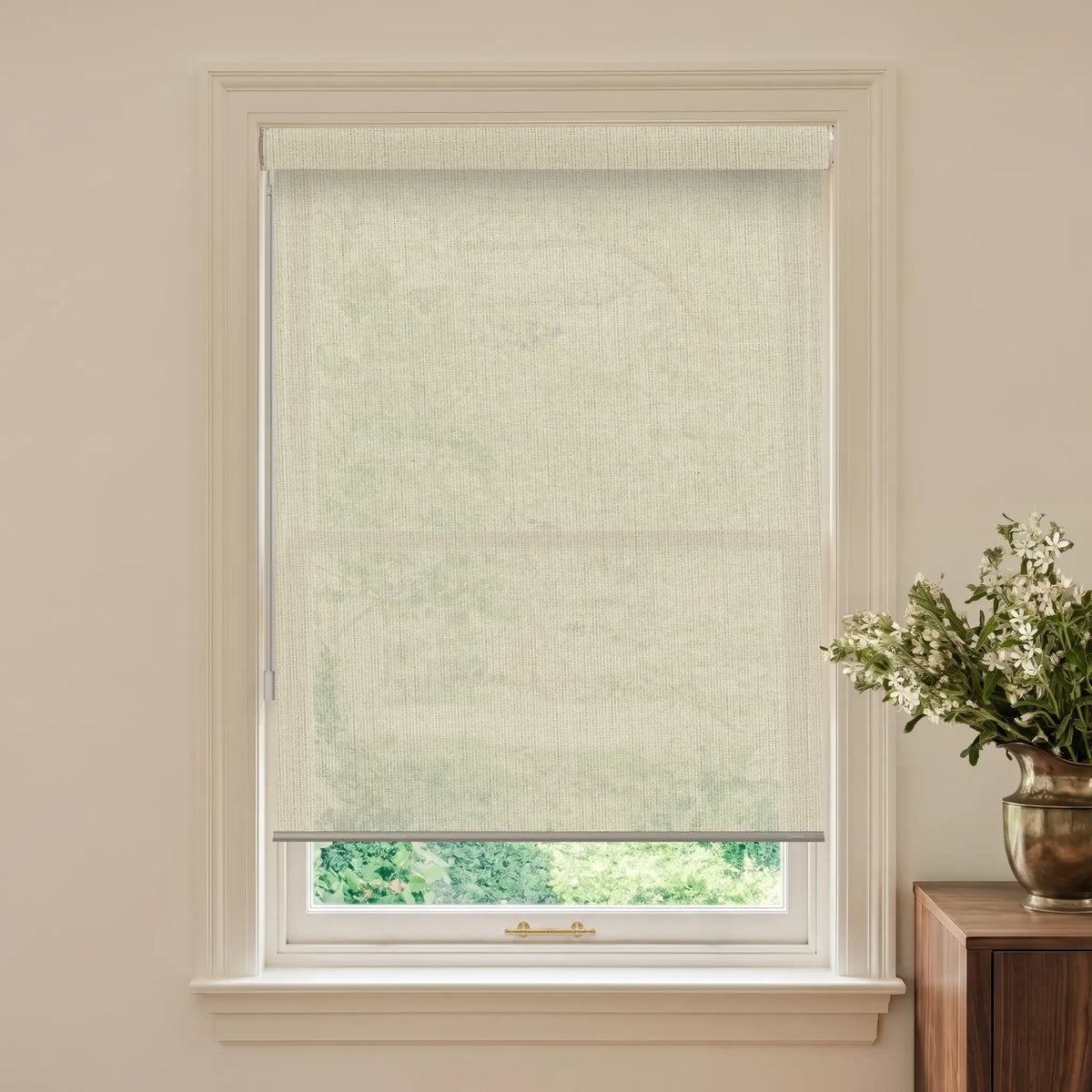 Window with a light-colored blind and a vase of flowers on a wooden cabinet.