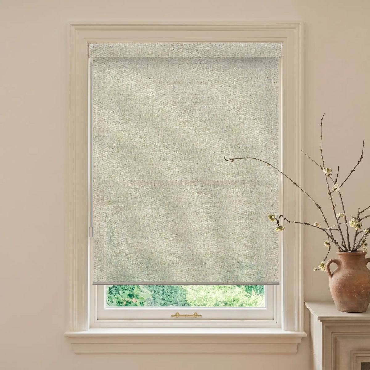 Window with a light green roller blind, beige walls, and a vase with branches on a windowsill.