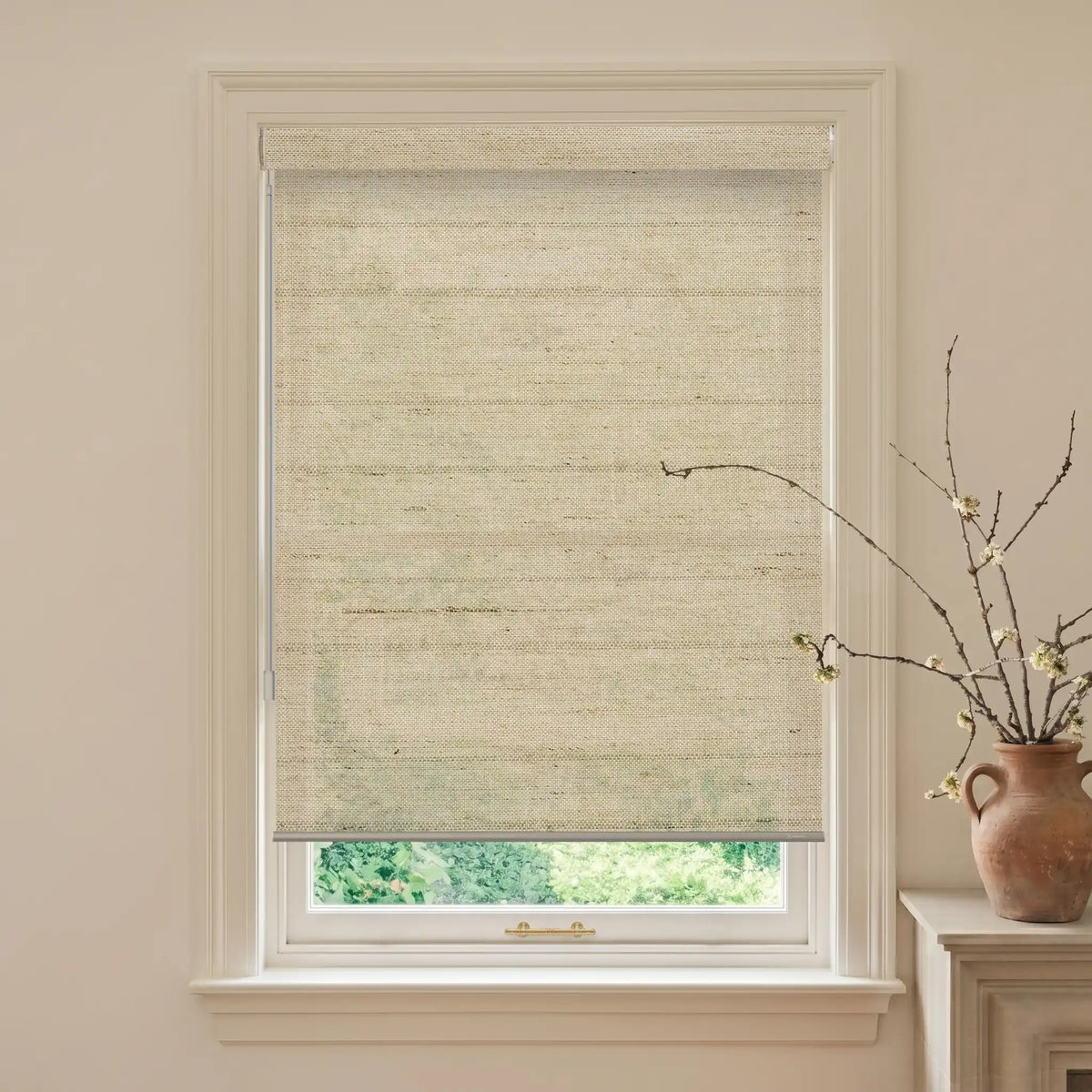 Window with beige woven blind and a vase with branches on a windowsill.