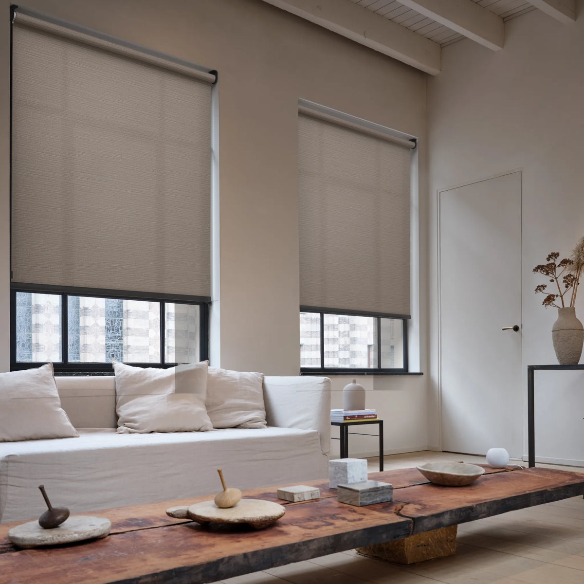Living room with beige light filtering roller shades on windows, white sofa, and wooden coffee table.