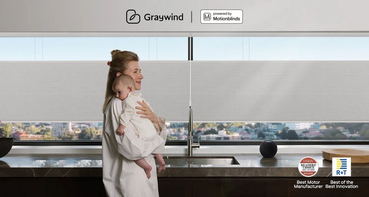 A woman holding a baby in a modern kitchen with motorized top down bottom up shades by Graywind × Motionblinds.