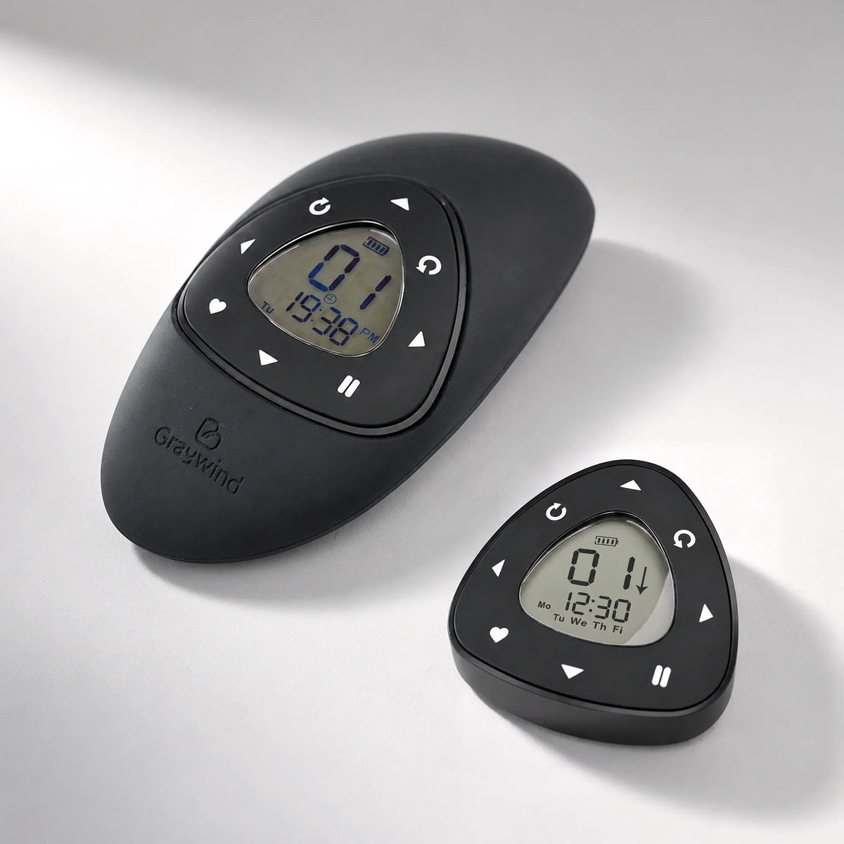 Two Graywind electronic wind-up keychains in matte black plastic, one larger oval-shaped unit and one smaller triangular unit, both with digital LCD displays and control buttons, shown on a light gray background.