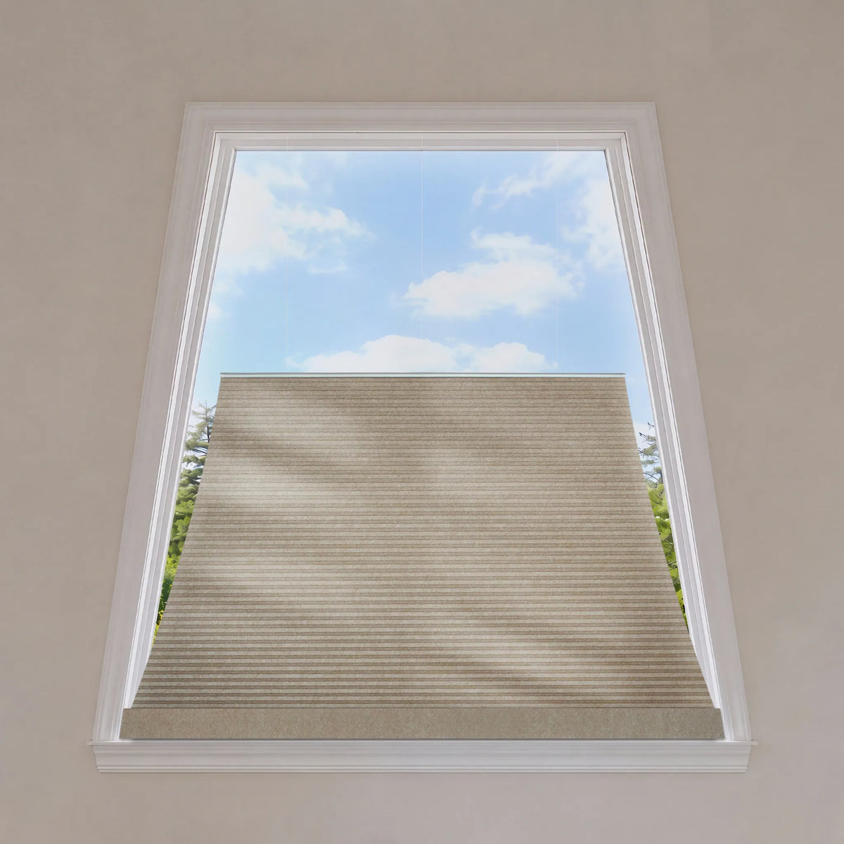 A beige trapezoid window shade partially drawn across a white-framed skylight, with a blue sky and clouds visible above and a bit of greenery at the sides.