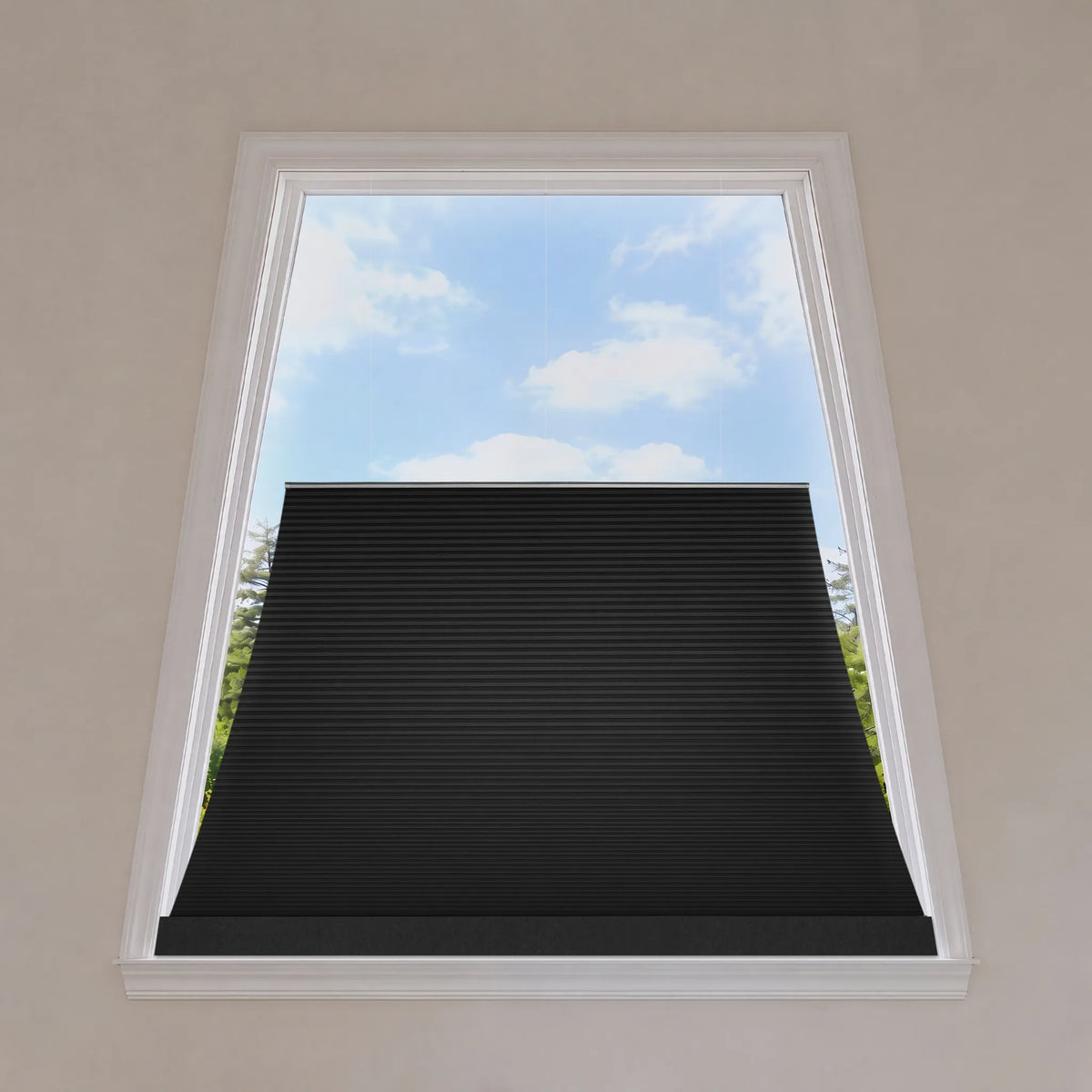A black trapezoid window shade partially drawn down over a white-framed window, with a view of blue sky and green trees outside.