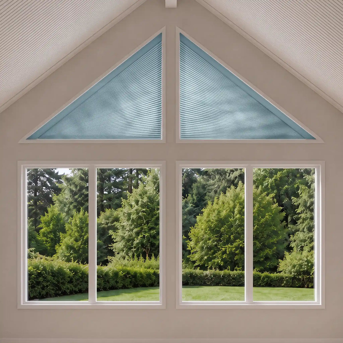 A set of light blue triangular cellular shades installed in a house, shown with two large triangular shades above a four-pane window looking out onto a green garden.