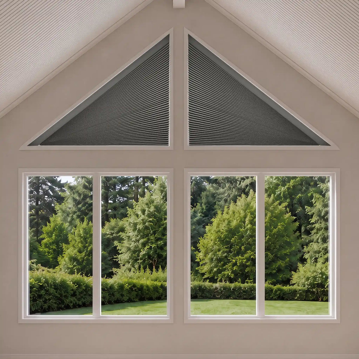 A set of dark gray triangular window blinds installed in a gable-shaped section above four smaller windows, showing a lush green garden outside. The interior wall is a warm beige tone.