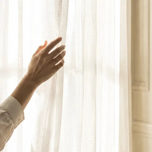 Hand gently touching sheer curtain fabric in soft natural light