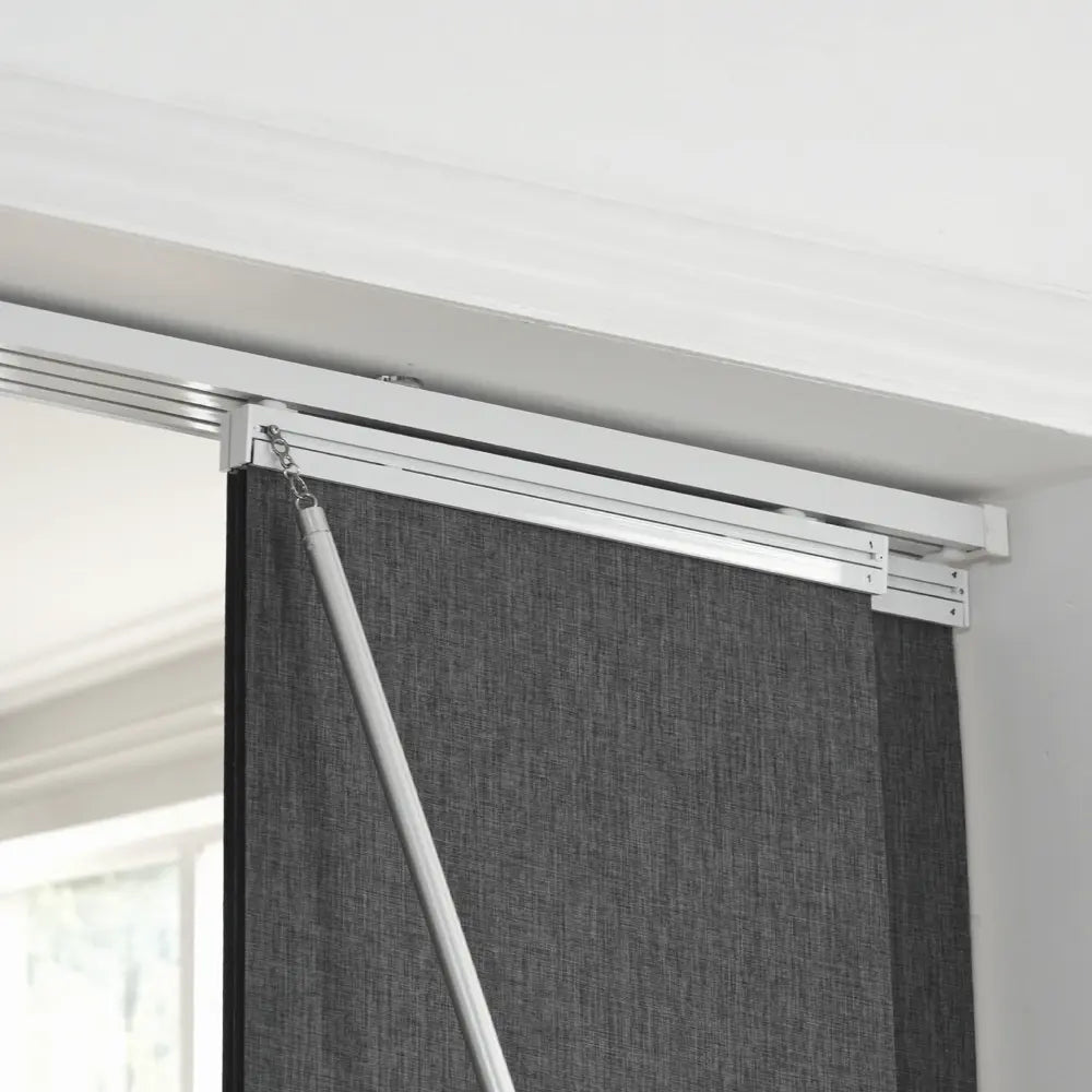 A dark gray textured panel track blinds inside mounted on a white metal track system, shown in a home interior setting.