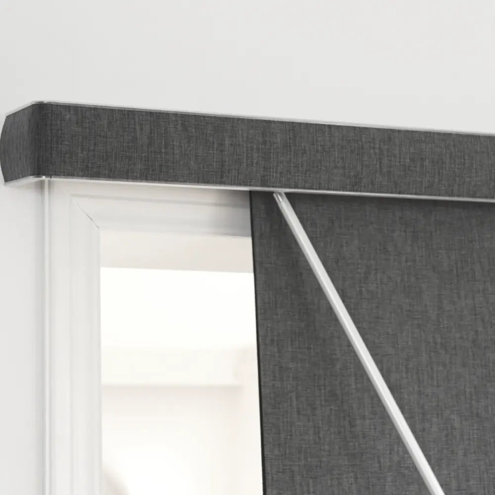 A close-up of a dark gray textured panel track blinds partially drawn across a window, showing the fabric texture, white frame, and support rod.
