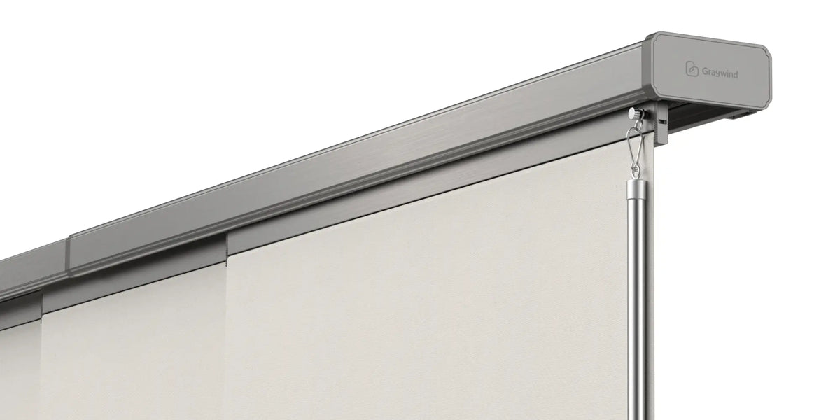 A close-up of a retractable manual panel track blinds showing the top rail, hanging pole, and part of the white screen fabric against a light gray background.