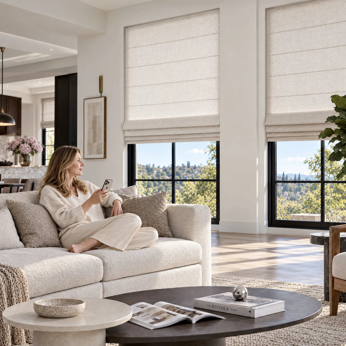 A person using a smartphone beside plain fold roman shades in a living room.