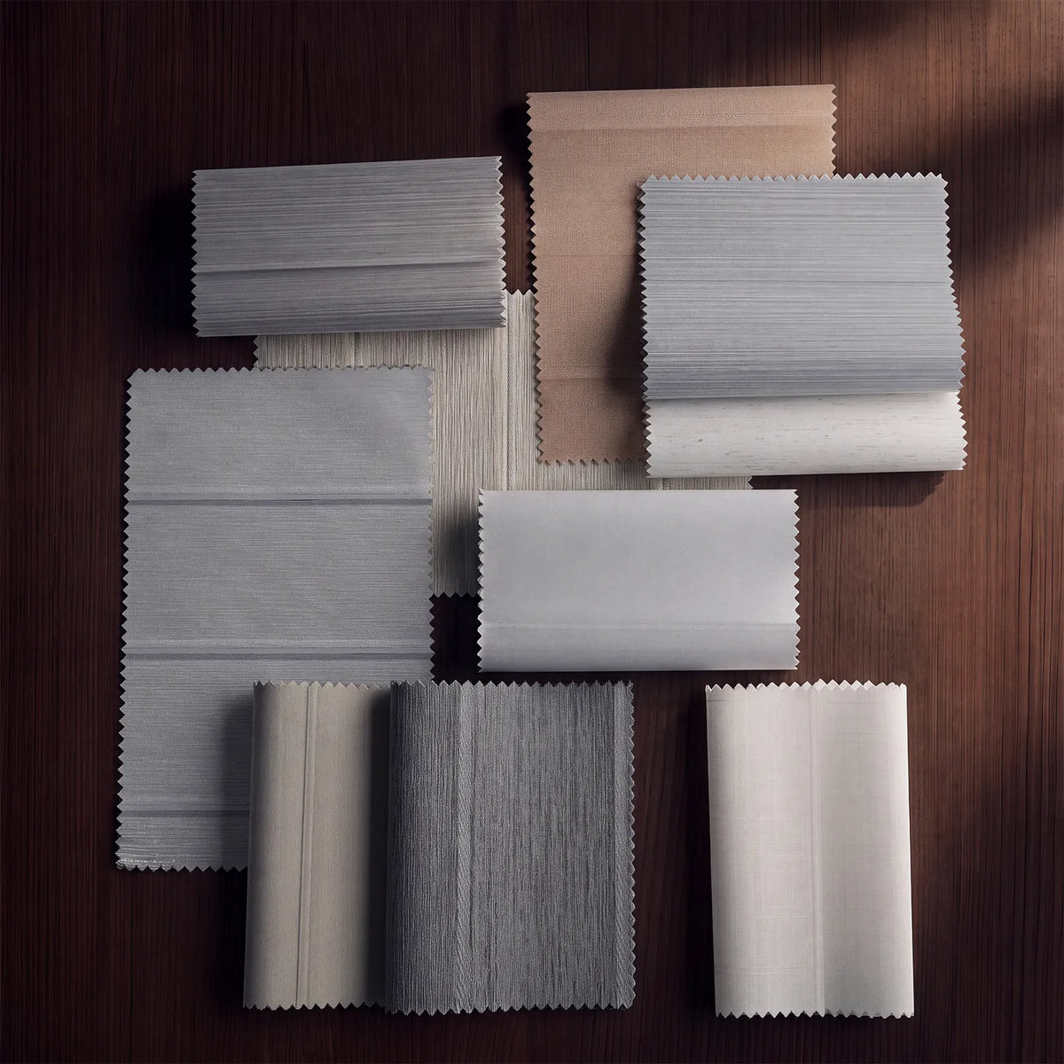 A set of fabric or material swatches in neutral tones, including white, light gray, beige, and charcoal, arranged on a dark wood background.
