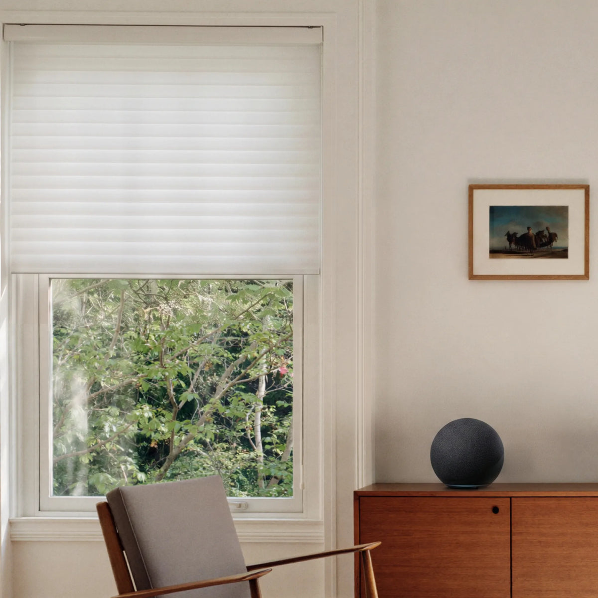 A white shangrila shade with horizontal slats partially drawn across a window in a modern room setting, with a wooden chair, a wooden cabinet, and a framed picture on the wall.