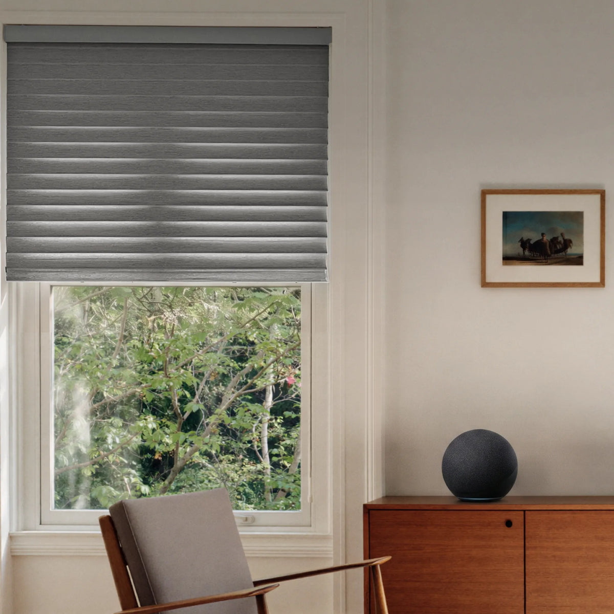A gray pleated roller blind partially drawn over a window in a modern living room setting with a wooden chair, cabinet, and framed picture.