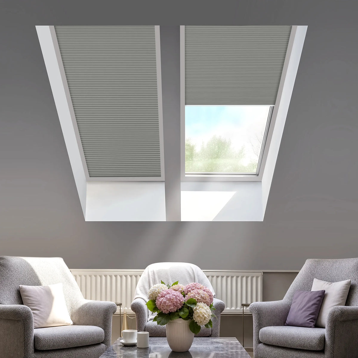 Two gray cellular roller blind skylights installed on a gray sloped ceiling of a modern living room with gray armchairs and a coffee table.