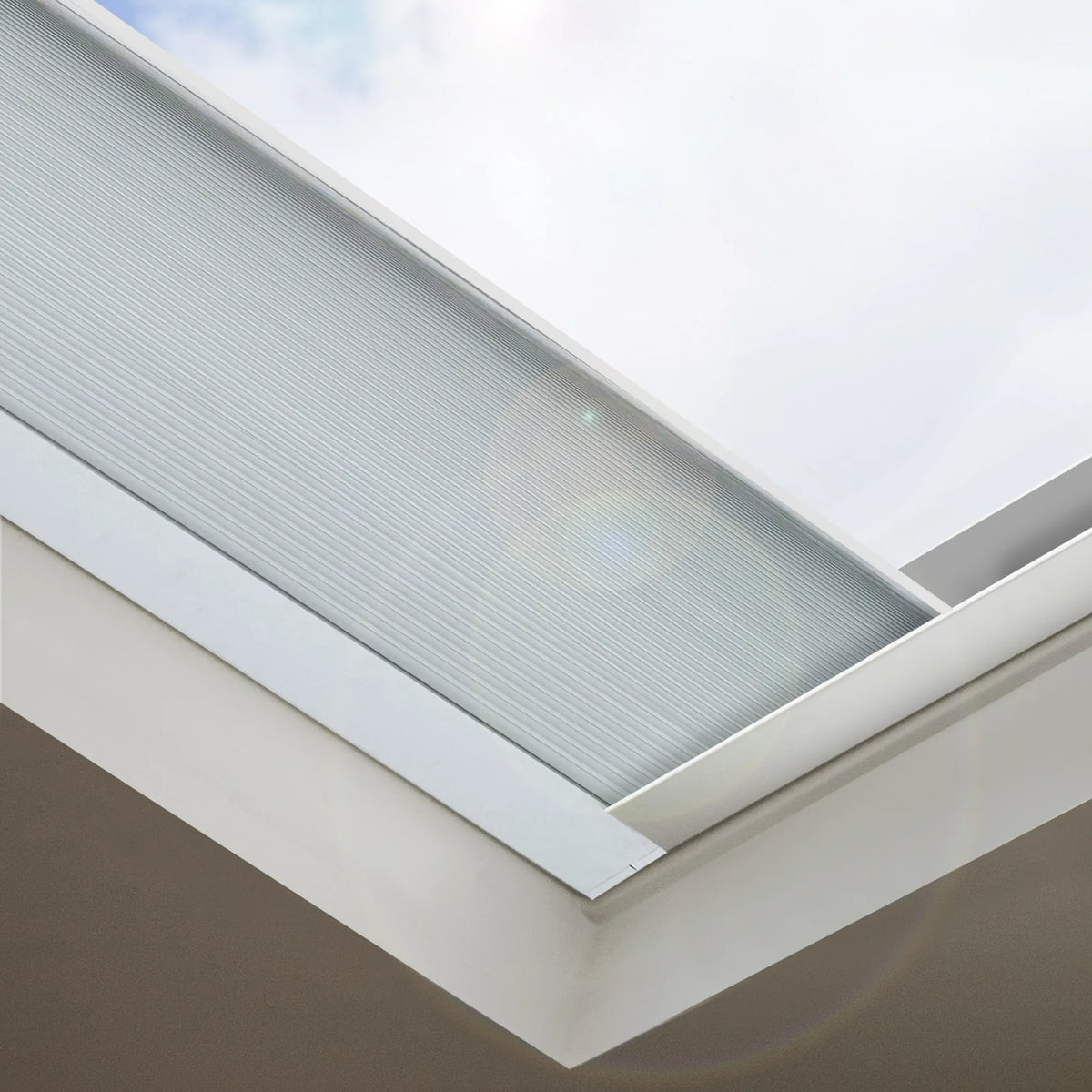 Close-up of a skylight window with a white frame and translucent textured glass panel, showing part of the exterior sky and interior wall.