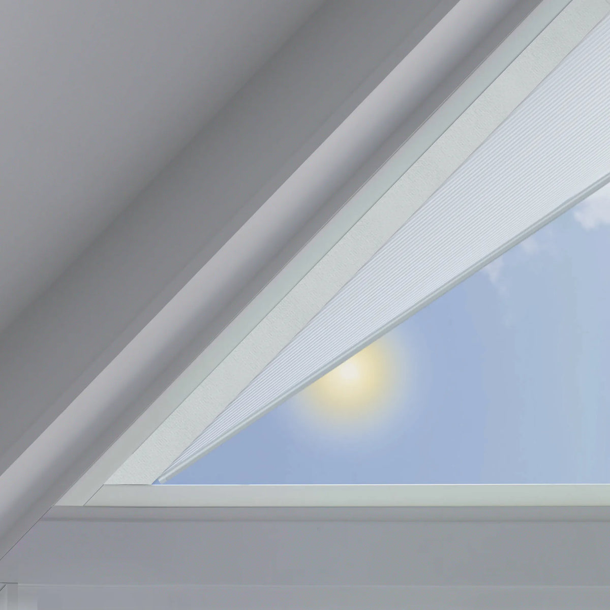 A close-up view of a white triangular cellular shades partially drawn across a triangular skylight, with a bright sun and blue sky visible outside.